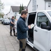 Ein Handwerkstechniker nutzt auf einem Tablet vor seinem Einsatzfahrzeug eine digitale Routen- und Tourenplanung.